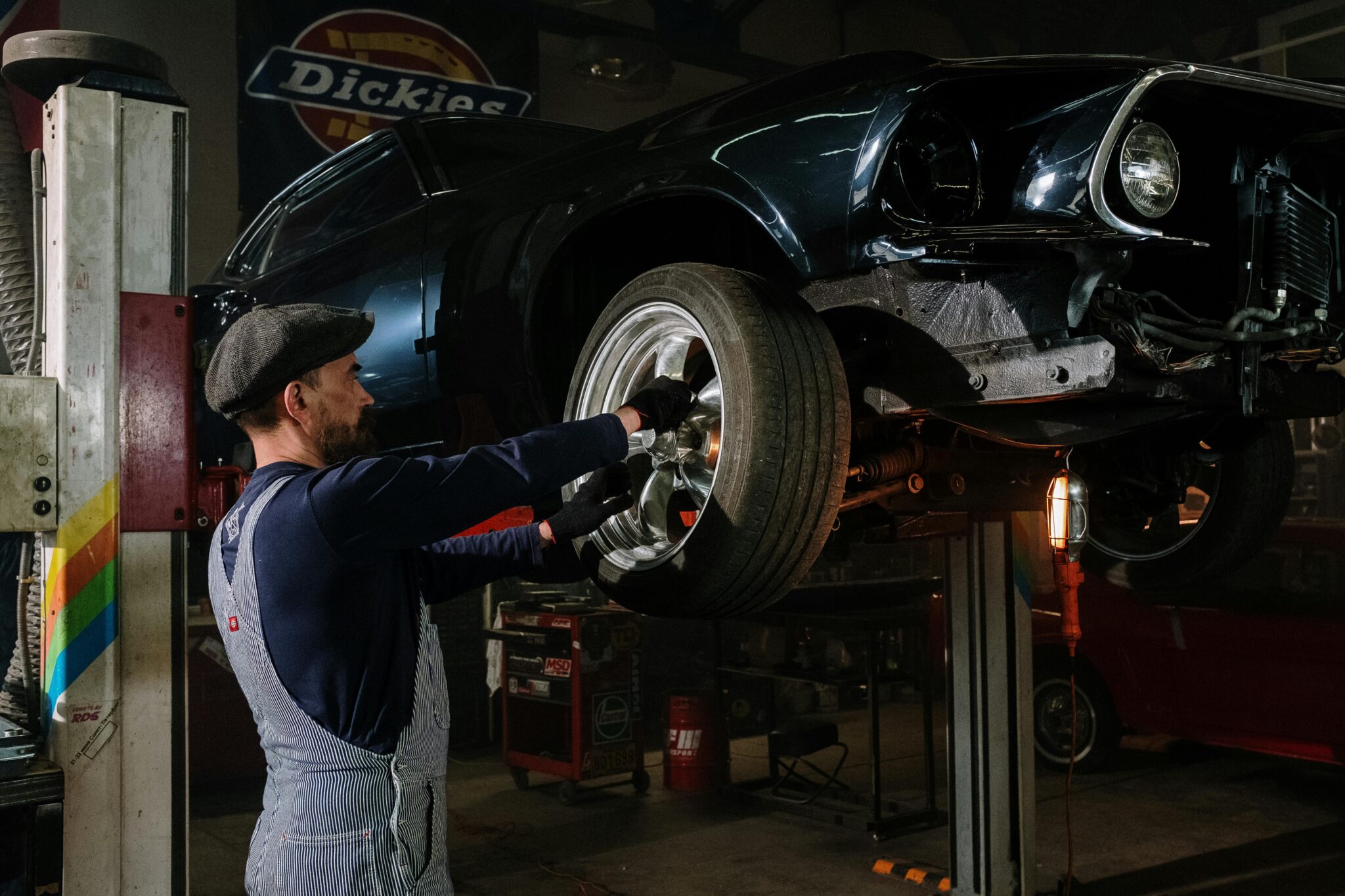 A focused mechanic works on a car wheel in a dimly lit garage, showcasing automotive repair skills.